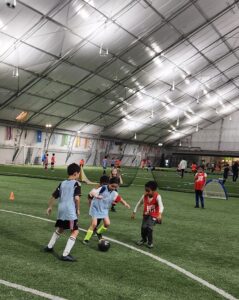 Kids playing soccer indoors on a turf field.