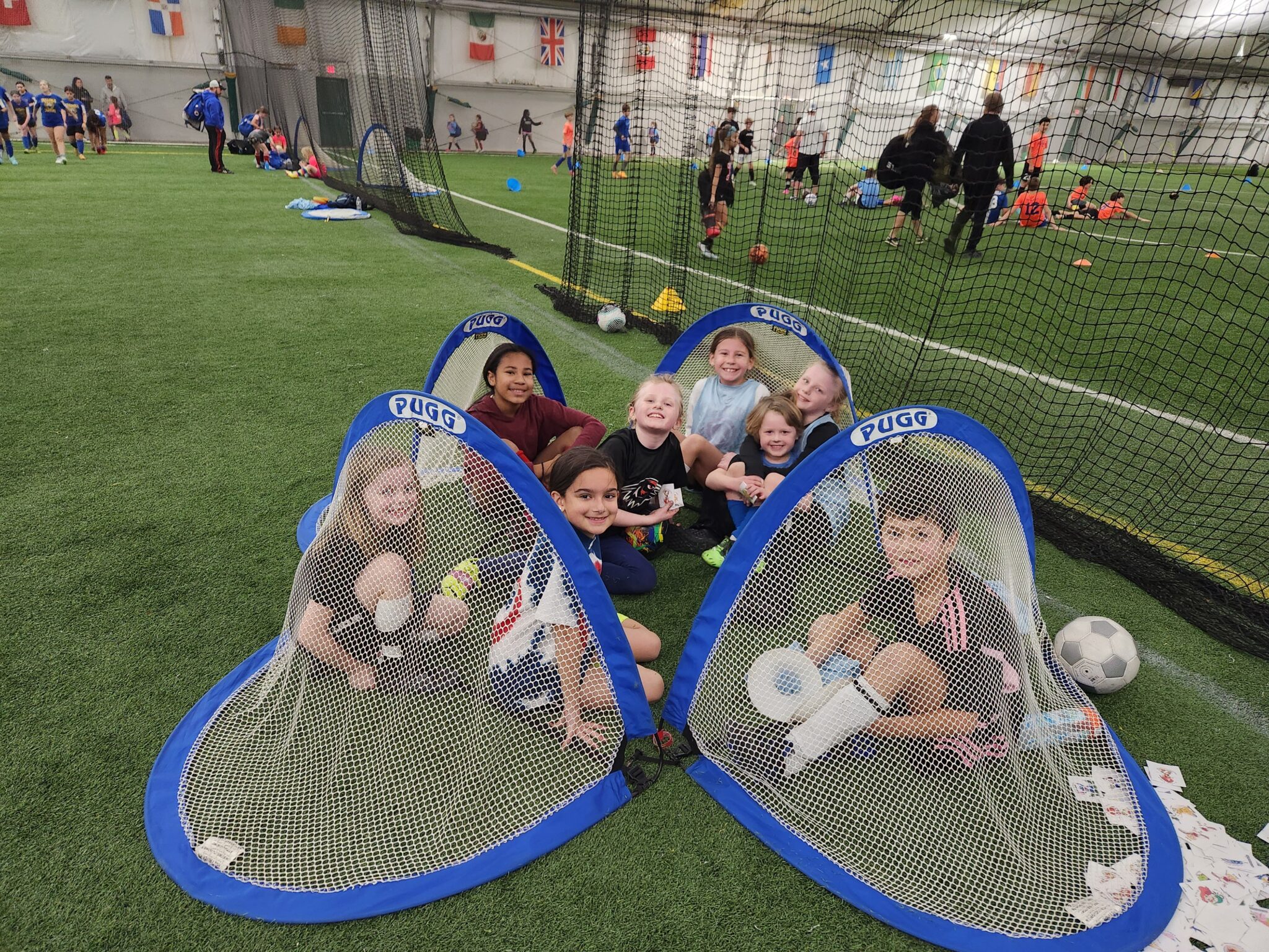 Kids posing happily inside mini soccer goals on an indoor field.