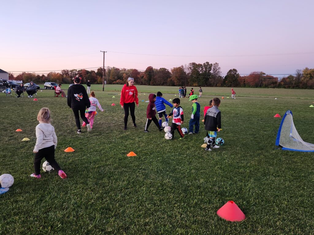 Children play soccer on a grassy field during sunset.