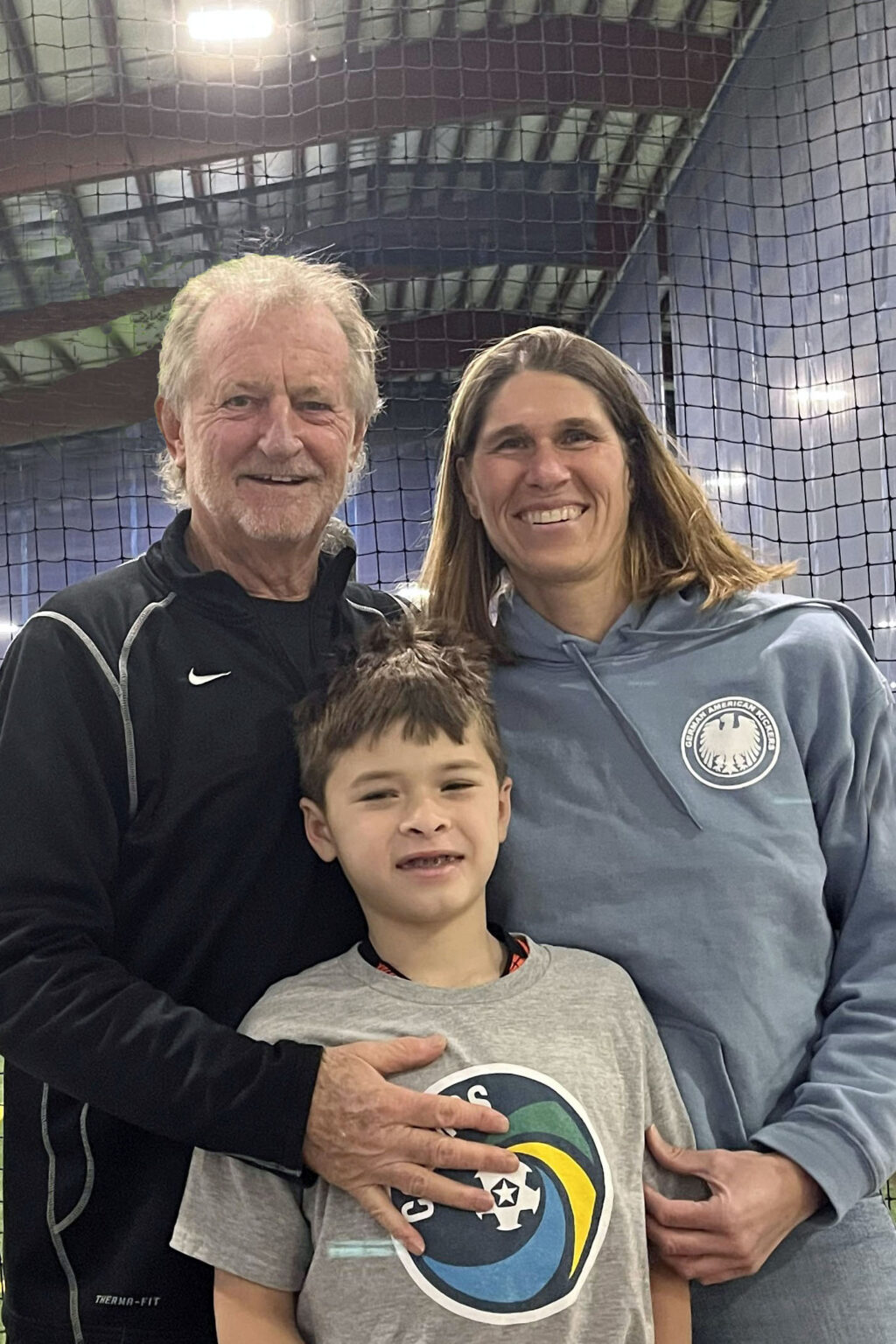 Three smiling people posing indoors, likely a family.