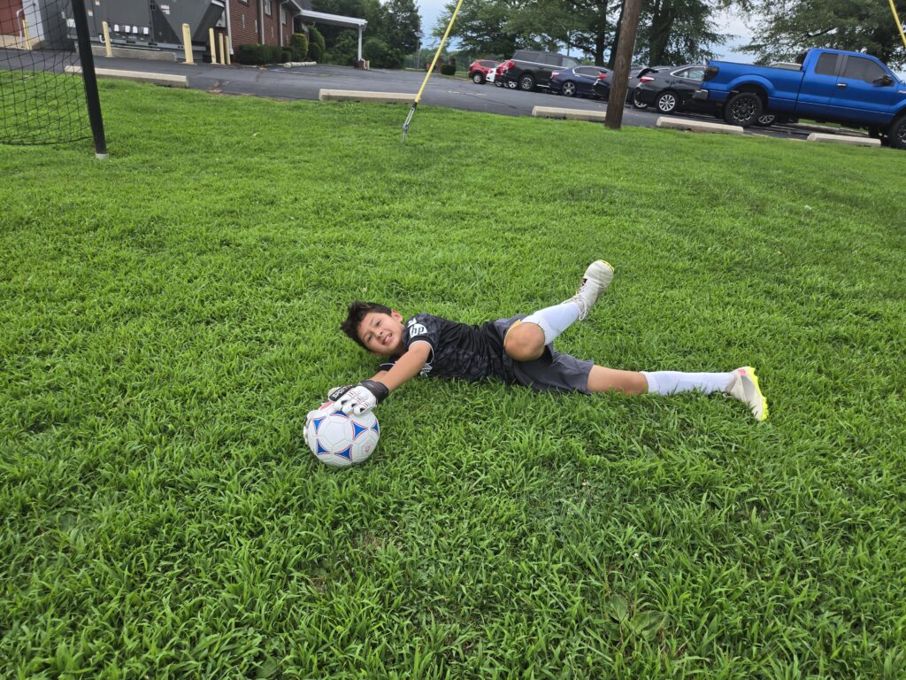 Girl lying on grass playing with a soccer ball.